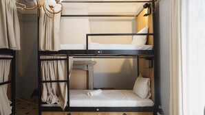 Habitación con literas, una litera inferior de madera y una superior blanca, junto a un pequeño armario de madera.