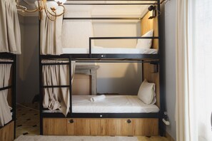 A bunk bed room with a wooden lower bunk, a white upper bunk, and a small desk with a chair.