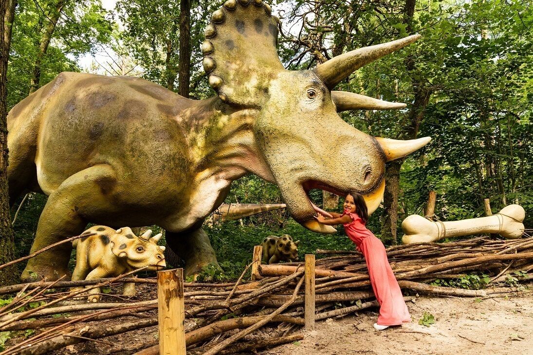 Eine große Dinosaurierstatue inmitten eines bewaldeten Gebietes, ein Kind interagiert damit.
