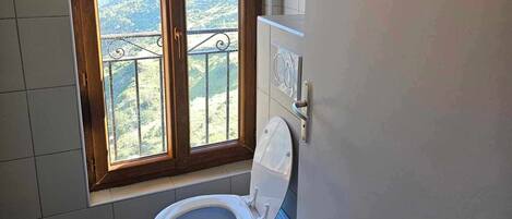 Un baño con inodoro, ventana con vistas a un paisaje montañoso y paredes con azulejos.