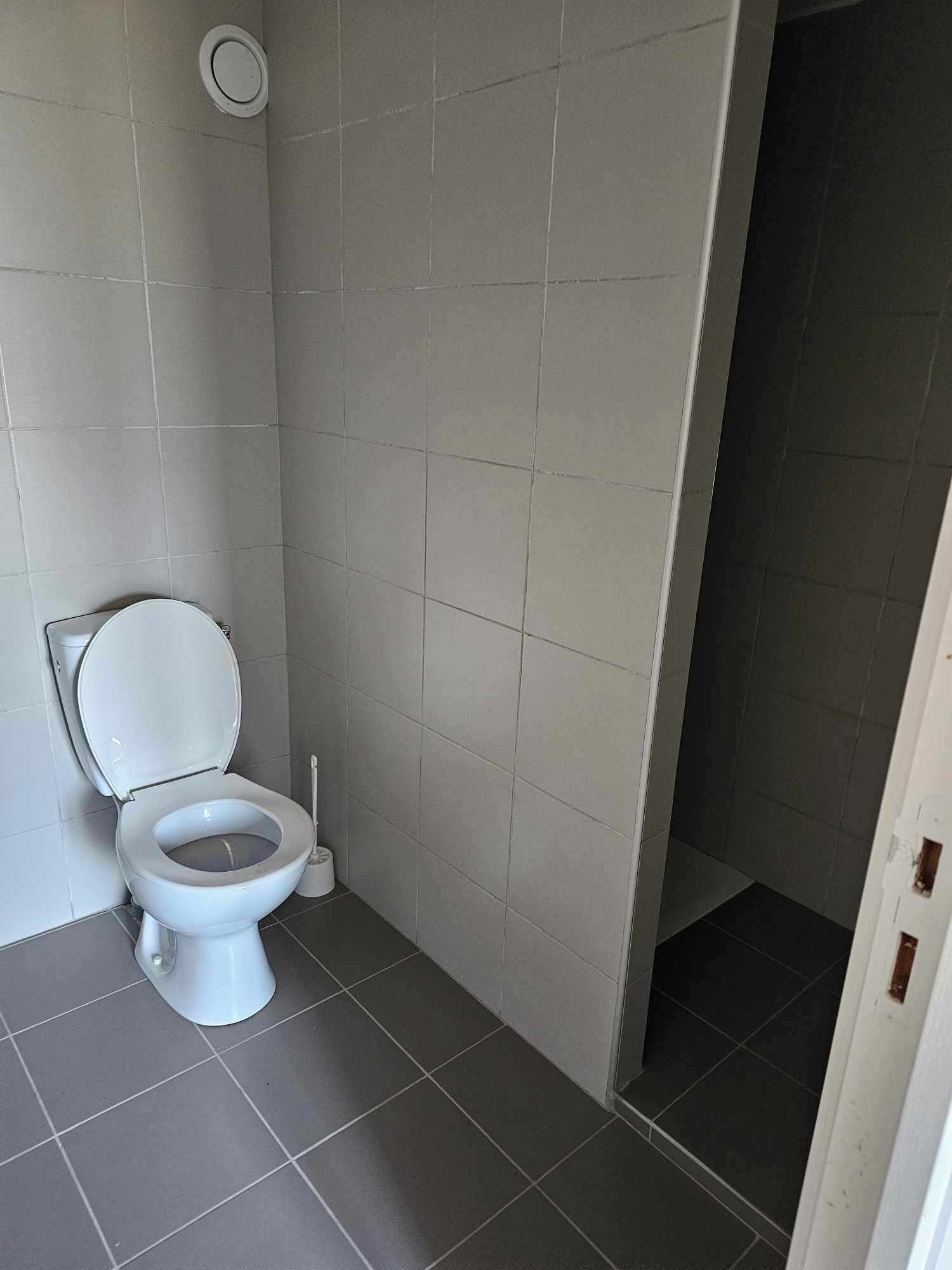 A small, clean bathroom with a white toilet, grey tiles, and a visible door frame.