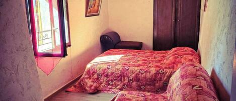 A bedroom with two beds, wooden ceiling beams, a window with curtains, and a door.
