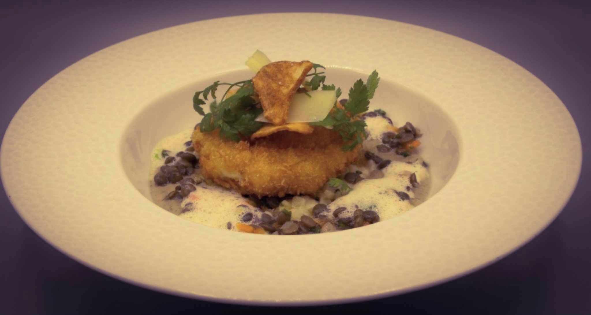 A dish with a golden-brown crust, garnished with green herbs and a slice of lemon, served on a white plate.