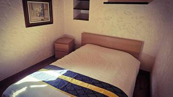Un dormitorio con cama, mesita de noche, un cuadro enmarcado en la pared y estantes empotrados.