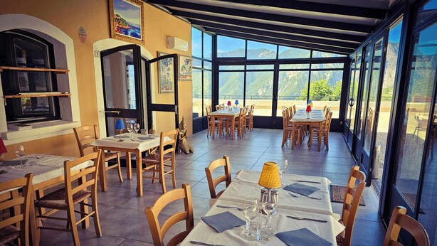 A restaurant with multiple tables and chairs, large windows offering a view of the mountains. - l'Auberge La Gruppio (Ilonse)