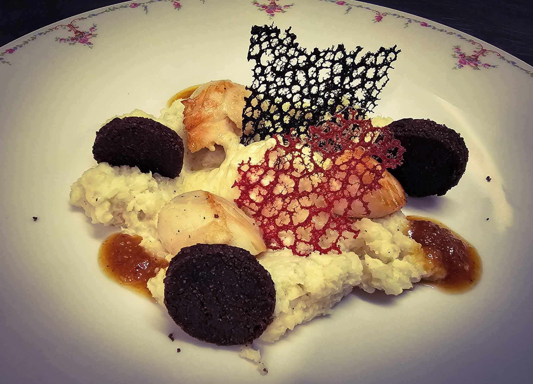 A plate with various food items including a piece of salmon, a dark round item, and a decorative element.