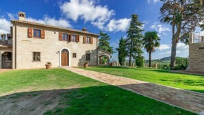A stone building with a paved driveway, a grassy lawn, and a view of the surrounding landscape.
