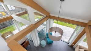 Un interno moderno con una scala che conduce a un balcone, una lampada a sospensione e un'area salotto con cuscini.