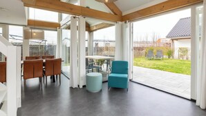 Un'ampia zona giorno con un'ampia porta scorrevole in vetro che dà su un patio, un'area pranzo con sedie e una poltrona blu.