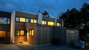 A modern two-story house with a wooden facade, a garage, and a paved driveway. - Holidayhouse - Lepelblad 42 | Nieuwvliet-Bad (Nieuwvliet)