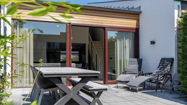 An outdoor patio with a table and chairs, a sliding glass door, and a white wall. - Holidayhouse - Lepelblad 42 | Nieuwvliet-Bad (Nieuwvliet)