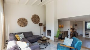 A spacious living area with a grey sofa, a blue armchair, and a coffee table. There are two wall art pieces and a floor lamp. - Holidayhouse - Lepelblad 42 | Nieuwvliet-Bad (Nieuwvliet)