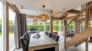 A dining area with a wooden table and chairs, large windows, and a staircase.