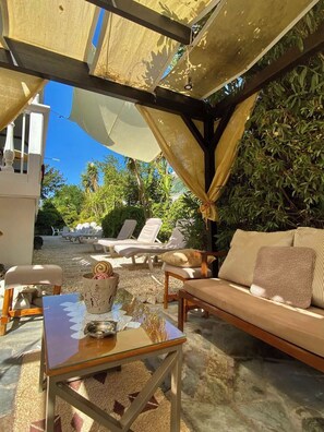 An outdoor seating area with a table, chairs, and a sofa under a shaded structure. - Marinos Rooms (Zakynthos)