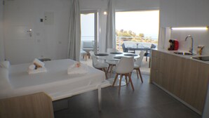 Une chambre d’hôtel moderne comprenant un lit, une table à manger avec des chaises, un coin cuisine et un balcon avec vue.