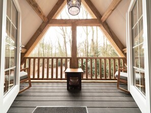Eine Holzdar Terrasse mit integriertem Kamin, Holzgeländern und großen Fenstern mit Blick auf Bäume.