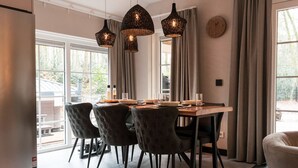 Een eetruimte met een houten tafel, vier gestoffeerde stoelen en drie hanglampen.