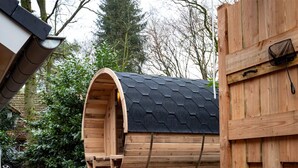 Een houten, vatvormige constructie met een zwart dak, een houten deur en een klein opstapje.
