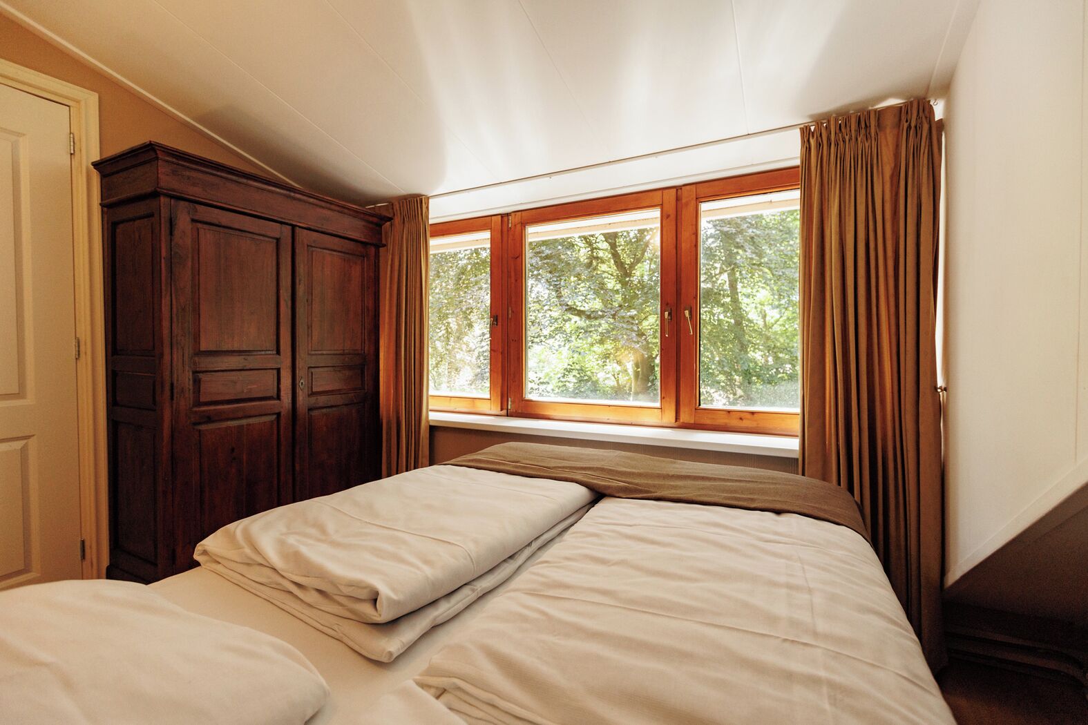 Une chambre avec deux lits, une armoire en bois et une fenêtre avec des rideaux.