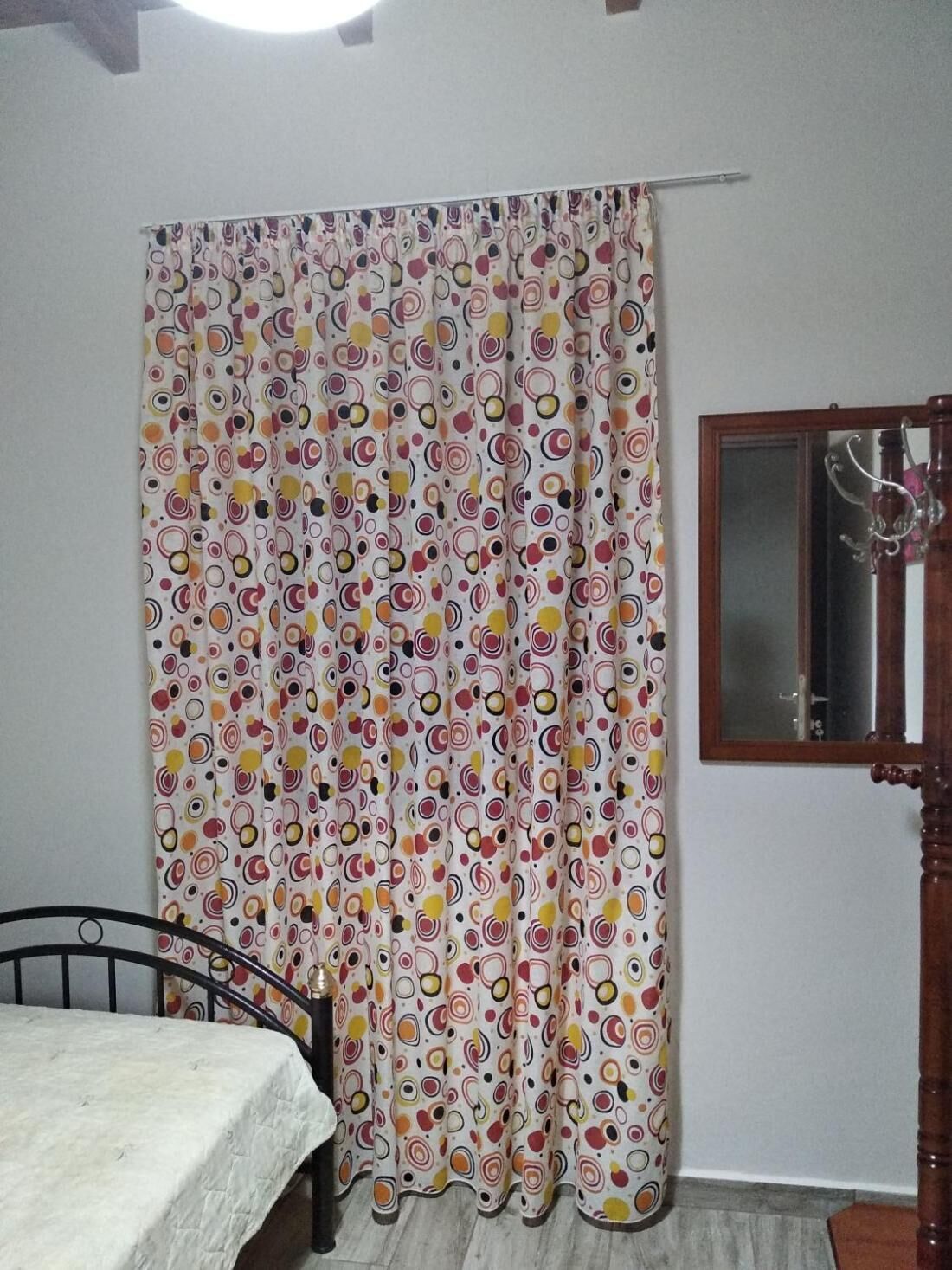 Une pièce avec un lit, une fenêtre avec un miroir et un rideau orné d’un motif circulaire aux couleurs vives.