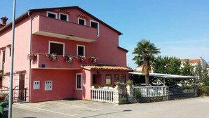 A pink two-story building with a balcony, a gated entrance, and a parking area.