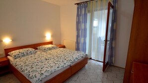 A bedroom with a double bed, bedside lamps, a radiator, and a window with curtains.