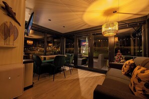 Un interior moderno con comedor, sofá y ventana grande con vista a un árbol de Navidad.