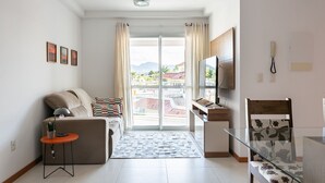 En moderne stue med en sofa, et lille bord med en lampe, et glasbord og et fjernsyn ophængt på væggen.