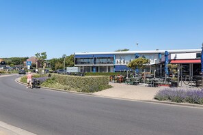A building with a blue and white facade, outdoor seating area with tables and chairs, and a pedestrian crossing sign.