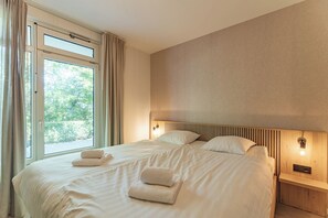 A hotel room with a large bed, two bedside lamps, and a window with curtains.