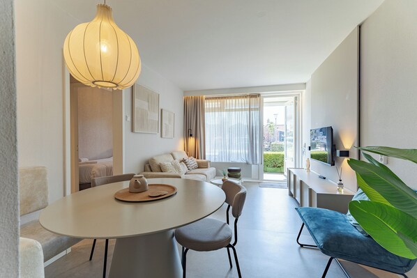 A modern living room with a dining table, chairs, a sofa, and a large plant.