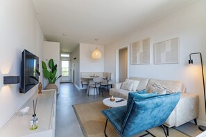 En moderne stue med sofa, en blå lænestol, et fjernsyn og et spiseområde med bord og stole.