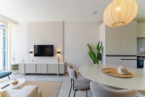 Un salon moderne doté d’un téléviseur à écran plat, d’une table à manger, de chaises et d’un coin cuisine.