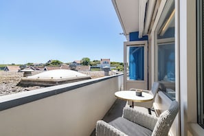 Ein Balkon mit Tisch und Stühlen, Blick aufs Meer und ein Gebäude im Hintergrund.