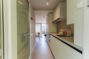 Eine schmale Küche mit Spüle, Herd und Fenster mit Blick auf eine Terrasse.