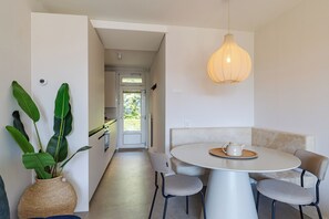 A modern dining area with a round table, two chairs, a hanging light fixture, and a potted plant.