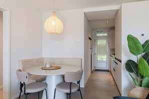 A dining area with a round table, four chairs, a hanging light fixture, and a door leading to another room.