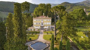 A large, yellow building with a symmetrical facade, surrounded by a well-manicured garden with a central pond and a pathway leading to the entrance.