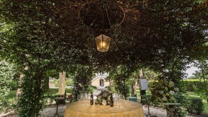 An outdoor dining area with a table set for a meal, surrounded by lush greenery and a hanging lantern.