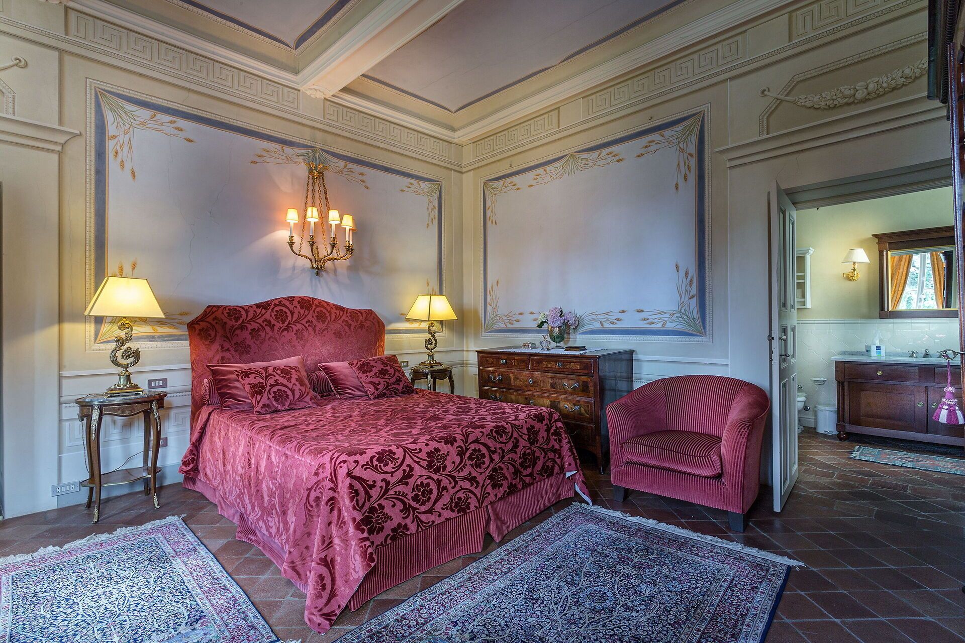 A spacious bedroom with a large bed, two bedside tables with lamps, a dresser, a chair, and a mirror.