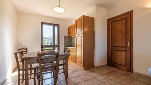 A dining area with a wooden table and chairs, a kitchen with wooden cabinets, and a door. - Casa Pompia 2 - Two Bedroom Apartment, Sleeps 4 (Siniscola)