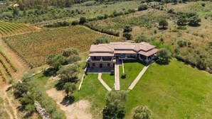 A large stone house with a tiled roof, surrounded by lush green fields and vineyards, set in a hilly landscape. - Casa Pompia 2 - Two Bedroom Apartment, Sleeps 4 (Siniscola)