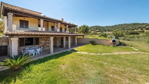 A two-story house with a patio area, stone columns, and a view of the surrounding landscape.