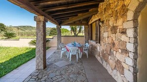 A covered outdoor patio with stone walls, a stone table with chairs, and a view of the surrounding landscape.