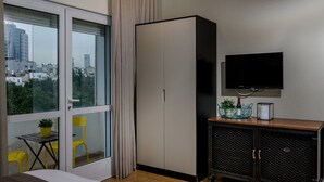 A hotel room with a large window, a wardrobe, a television, a small table with a plant, and a chair. - Dizengoff square boutique (Tel Aviv)