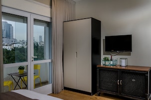 A hotel room with a large window, a wardrobe, a television, a small table with a plant, and a chair.