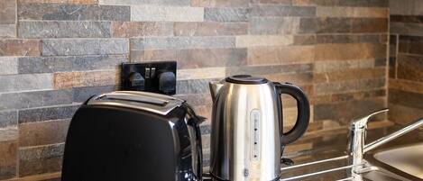 A kitchen with a toaster and a kettle on a countertop, a sink, and a tiled backsplash.
