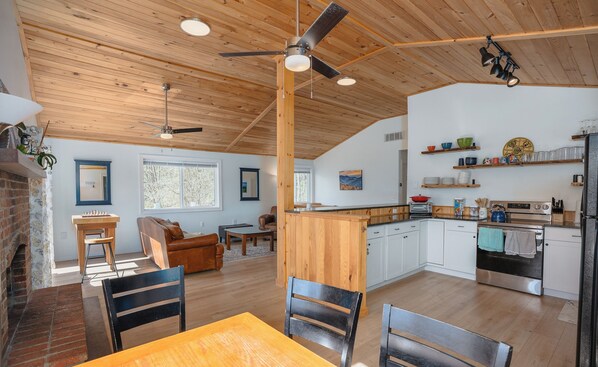 A spacious living area with a fireplace, a dining table, and a kitchen with white cabinets and wooden countertops. - River Retreat with Kayaks, Firepits, Stars (Strasburg)