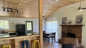A spacious living area with a fireplace, wooden ceiling, and a dining area with chairs and a table. - River Retreat with Kayaks, Firepits, Stars (Strasburg)
