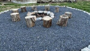 A circular fire pit surrounded by evenly spaced wooden stumps and a gravel border. - River Retreat with Kayaks, Firepits, Stars (Strasburg)